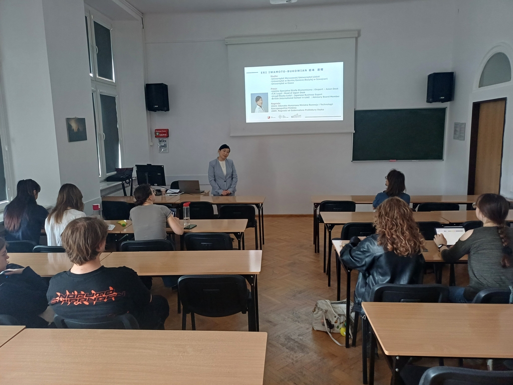 [Translate to English:] Prelegentka stojąca przed salą wykładową, prezentacja wyświetlana na ekranie z informacjami o jej doświadczeniu zawodowym; kilku studentów siedzi w ławkach i słucha.