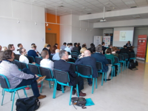 Conference attendees seated in the audience, listening to a speaker.
