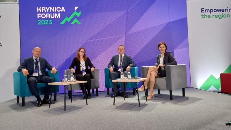 Dwóch mężczyzn i dwie kobiety siedzą przy dwóch stolikach na scenie podczas Forum w Krynicy/Two men and two women are sitting at two tables on the stage during the Forum in Krynica
