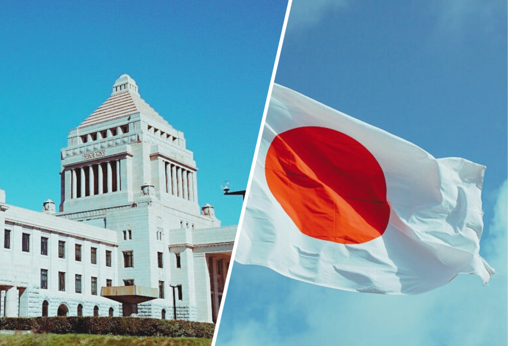 Po lewej stronie biały budynek na tle nieba, po prawej stronie powiewająca flaga Japonii na tle nieba